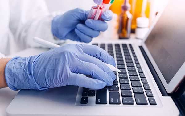 Researcher using a computer holding a couple of sample vials.